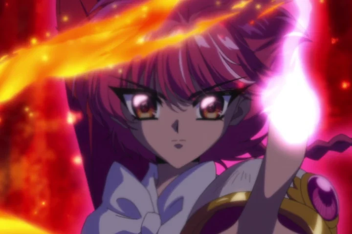 Hikaru aparece em primeiro plano com uma mão erguida diante de uma chama intensa, enquanto Umi e Fuu estão ao fundo.